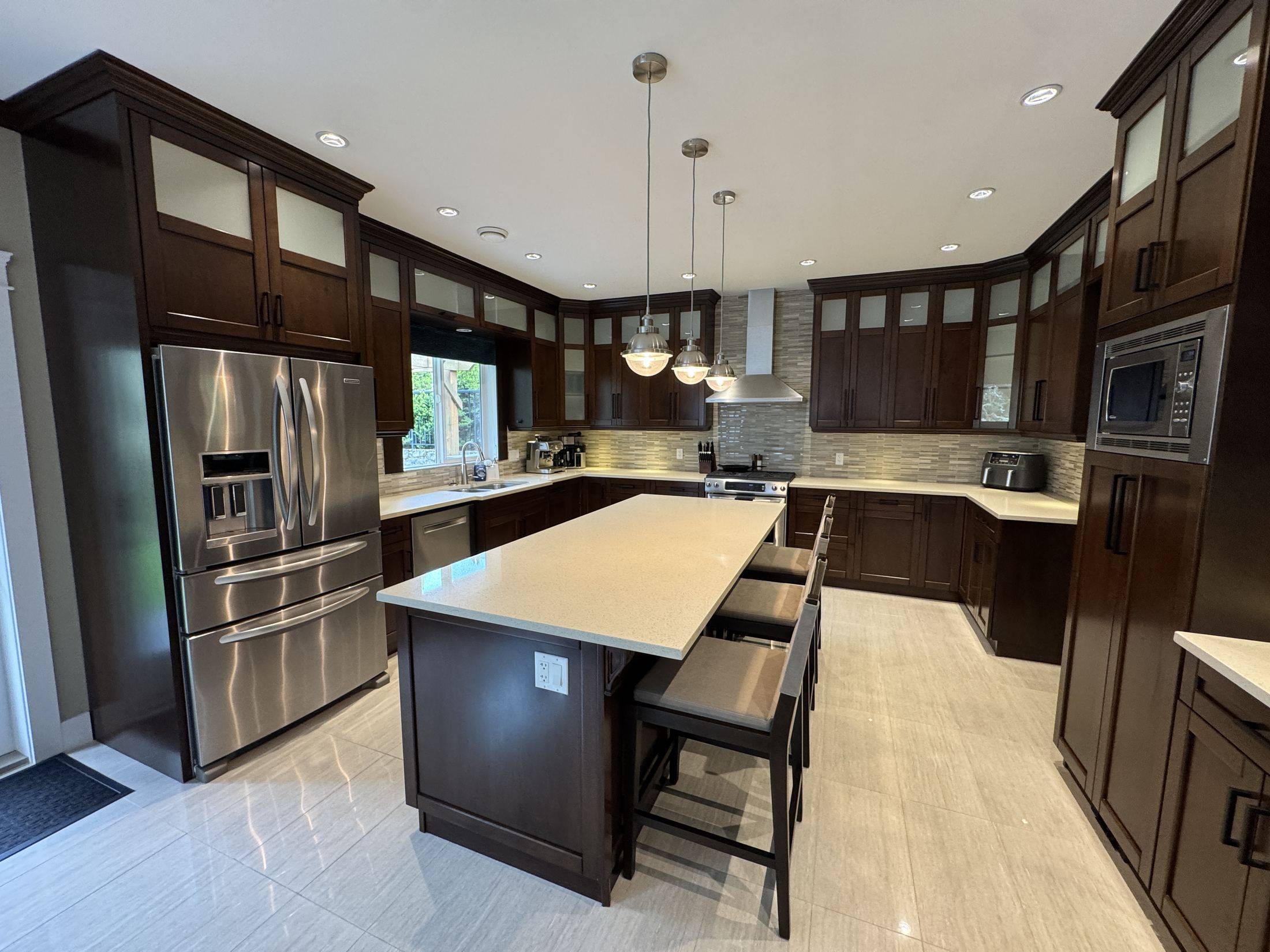 The kitchen: dark wood cabinetry, a long quartz island with three stools